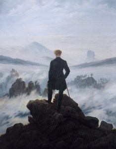 A man stands atop a mountain looking down at the clouds